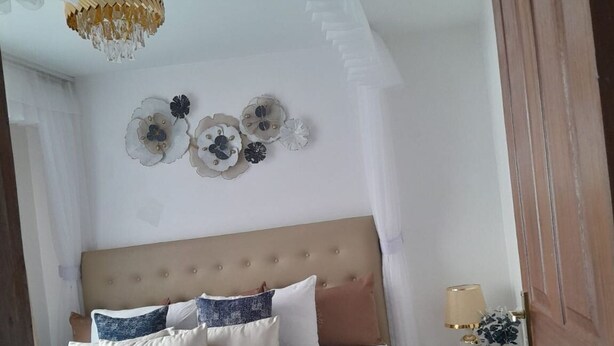 A bedroom with a bed, a nightstand, a lamp, and decorative wall art. - Lux Suites Zerubabel penthouse Kisumu (Kisumu)