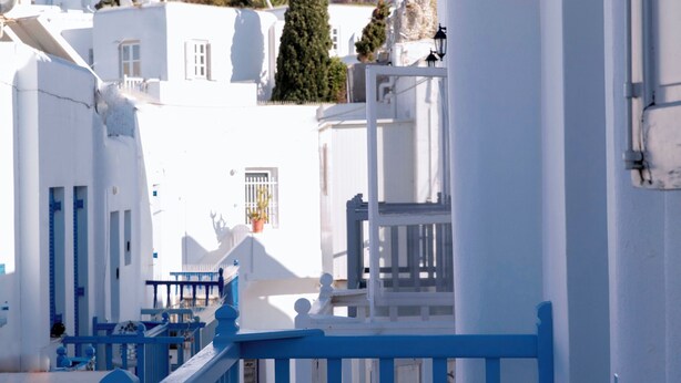 Un bâtiment blanc agrémenté de touches de bleu, avec un escalier et une vue sur une colline où se trouvent d’autres bâtiments.
