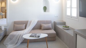 Un salon moderne avec un canapé beige, une petite table ronde sur laquelle repose un magazine, et une décoration minimaliste comprenant un cactus et un téléviseur posé sur un meuble.