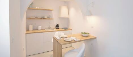A modern kitchen with white cabinetry, a wooden countertop, and a white bar stool.