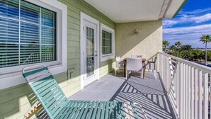 Un balcone con una sedia verde, un tavolo e una poltrona, con vista su un cielo sereno e palme.