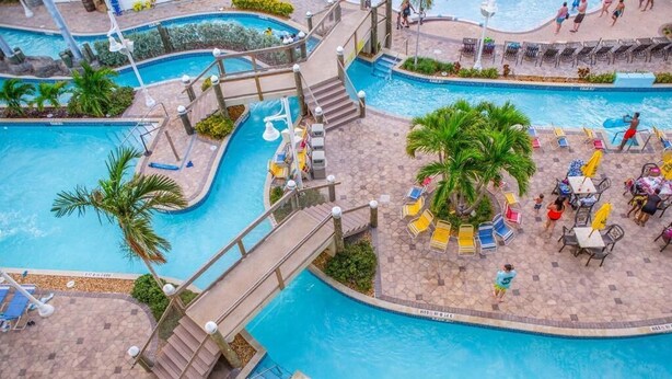 Una piscina a più livelli con un ponte che collega le varie sezioni, circondata da palme e zone relax.