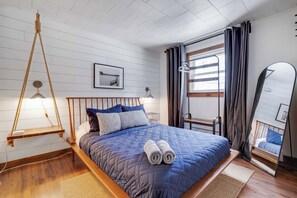 Une chambre à coucher avec un lit, un fauteuil suspendu, un miroir et une fenêtre avec des rideaux.