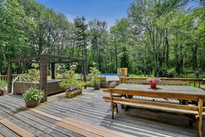 Une terrasse en bois avec un banc en bois et une table de pique-nique, entourée de plantes en pot et d’une pergola.