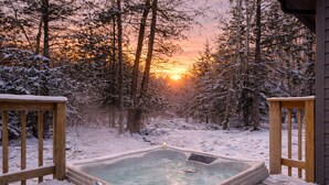 Ett bubbelbad i en snötäckt skog med en solnedgång i bakgrunden.