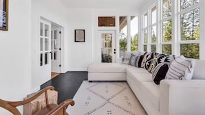 A spacious living room with a white sectional sofa, large windows, and a view of the outdoors.