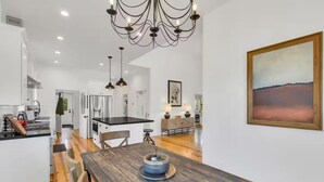 A modern kitchen with a wooden dining table, a chandelier, and a painting on the wall.