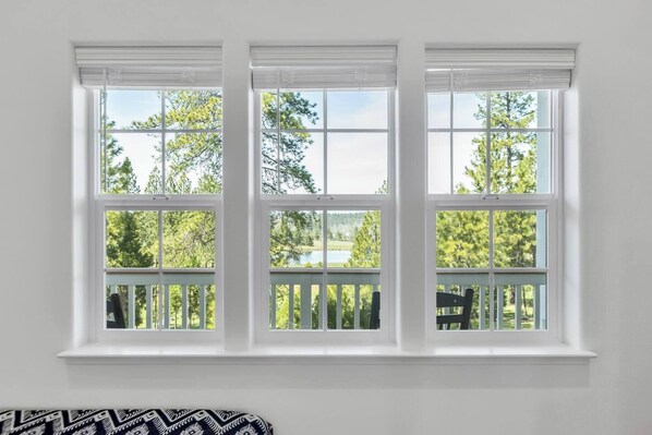 Una habitación con tres ventanas blancas y contraventanas blancas, una pared blanca y vistas a árboles y un lago.