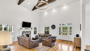 A spacious living room with a fireplace, leather sofas, a TV, and a large window.