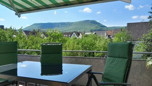 Una terraza con una mesa y sillas, un toldo a rayas, y vistas a casas y colinas.