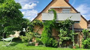 Una casa con techo inclinado, antena parabólica y jardín con hamaca.