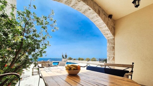 Una mesa de madera con un cuenco de fruta, asientos al aire libre y vista al mar.