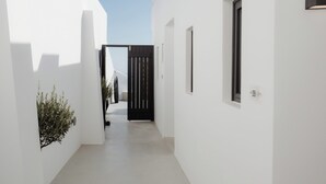 A narrow, white-walled corridor with a black door at the end, a small window with a number, and a potted plant on the left. - Serenity Suite Caldera View with Hot Tub (Thira - Santorini)