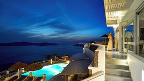 A poolside area with lounge chairs and umbrellas, overlooking a body of water at dusk. - Serenity Suite Caldera View with Hot Tub (Thira - Santorini)