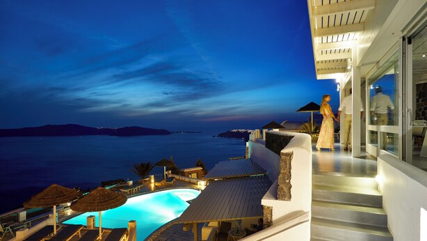 A poolside area with lounge chairs and umbrellas, overlooking a body of water at dusk. - Serenity Suite Caldera View with Hot Tub (Thira - Santorini)