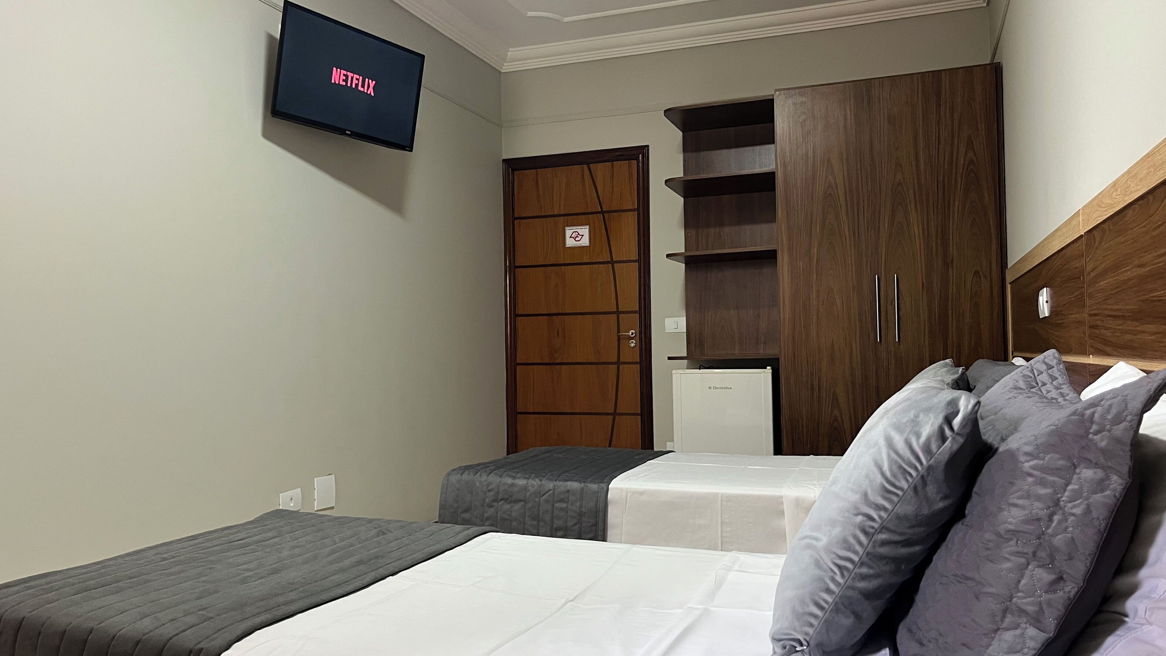 A hotel room with a bed, two bedside tables, a wardrobe, and a television displaying the Netflix logo.