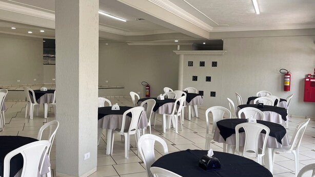Uma sala de conferências com cadeiras e mesas de plástico branco, um extintor e piso ladrilhado.