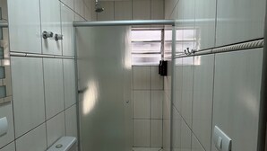 A bathroom with white tiled walls, a shower with a glass door, and a window providing natural light. - Gutierrez Hotel (Americana)
