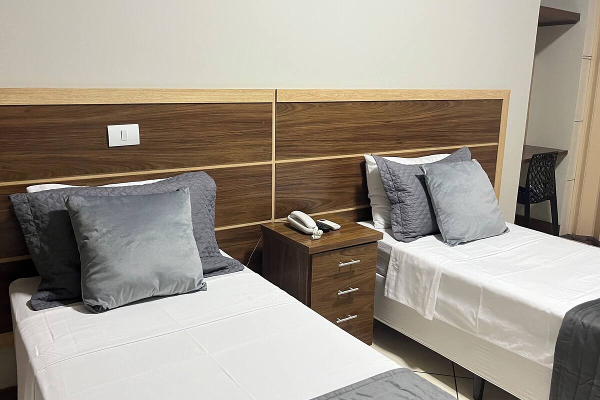 Two single beds with grey pillows, wooden headboards, and bedside tables with a phone and a lamp.