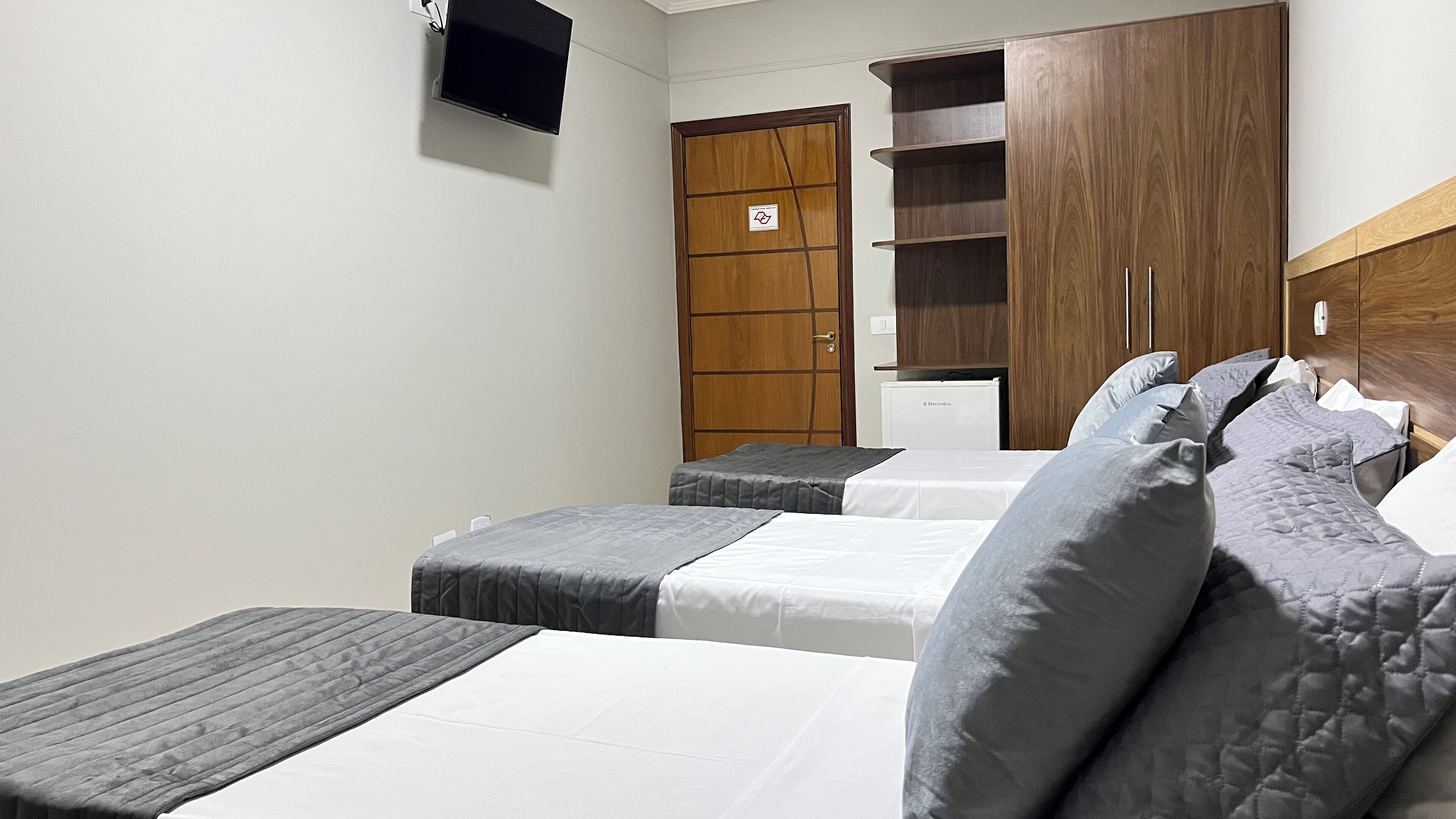 Quarto de hotel com duas camas, um guarda-roupa, uma pequena televisão e um radiador.