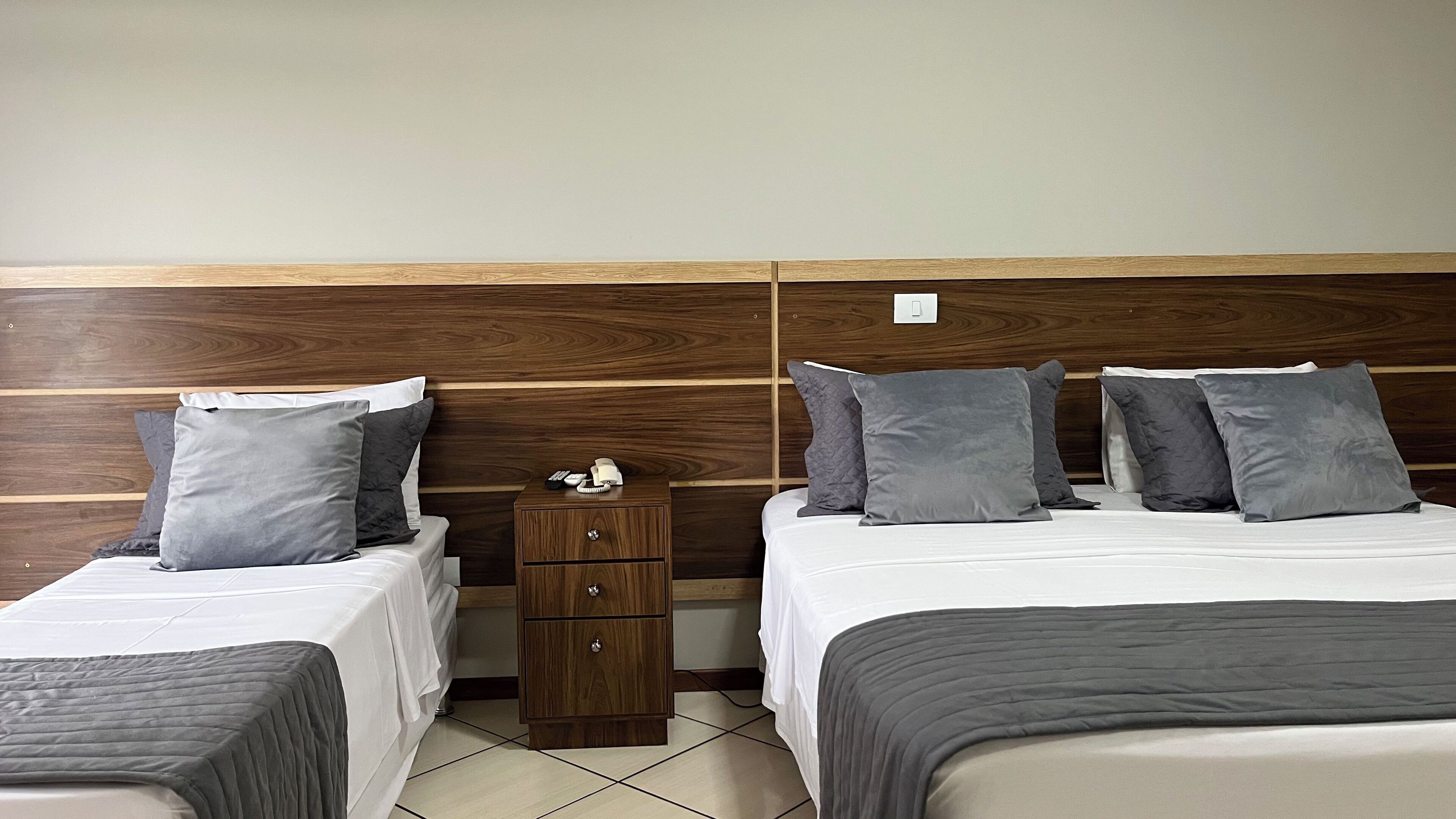 Une chambre d’hôtel avec deux lits, chacun doté de draps et d’oreillers gris, d’une tête de lit en bois et d’une petite table de chevet en bois avec une télécommande.
