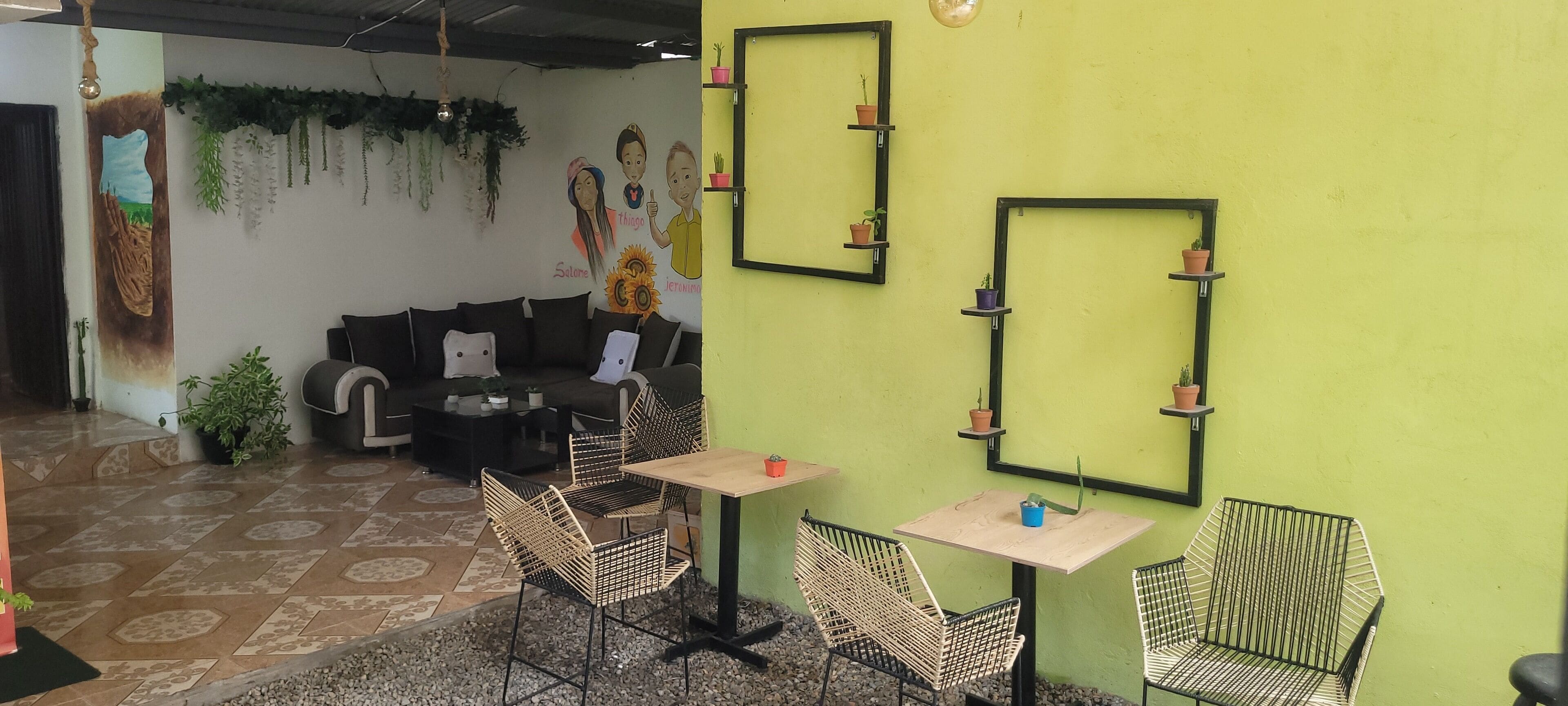 A cozy cafe with a green wall, black-framed mirrors, wicker chairs, and a black sofa.