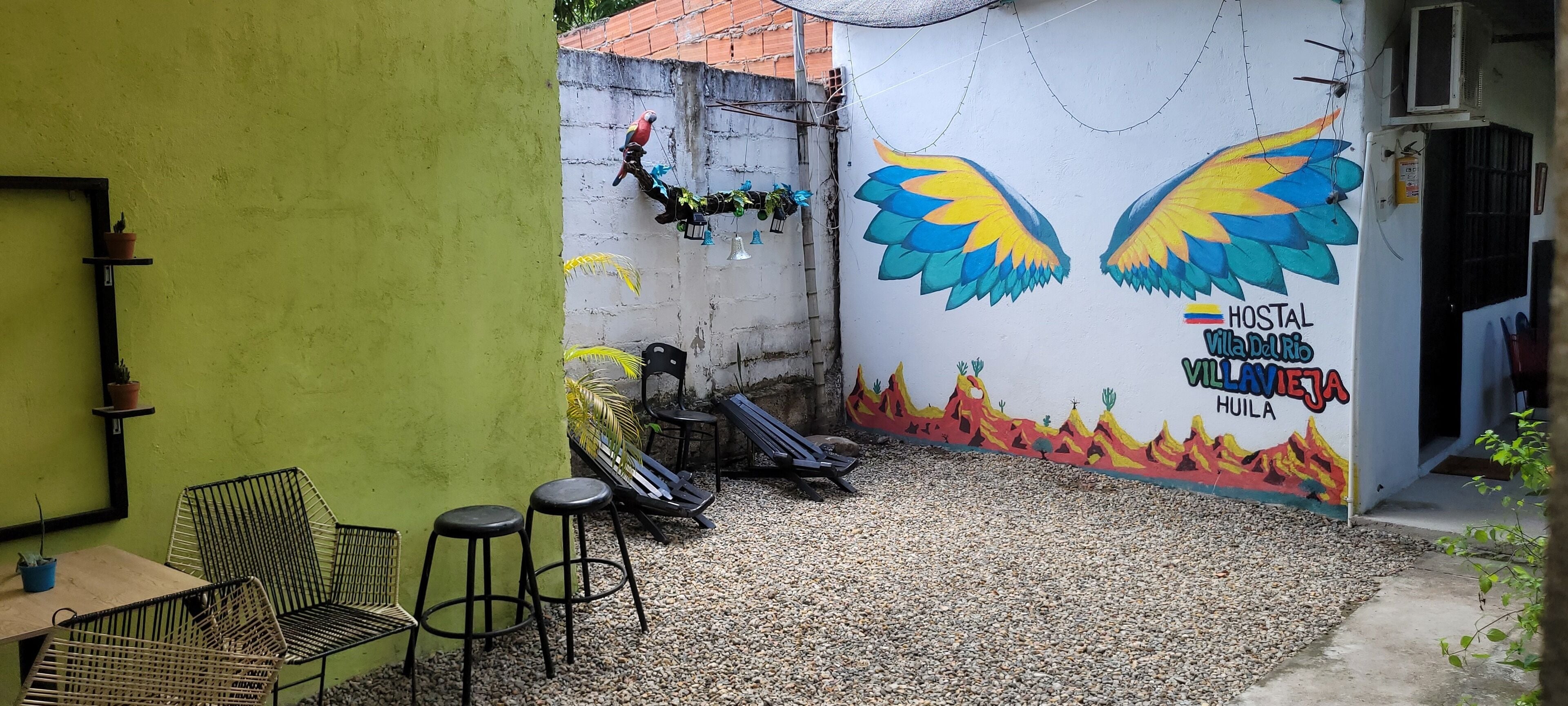 Un espace patio avec des sièges d’extérieur, une fresque murale et un climatiseur fixé au mur.