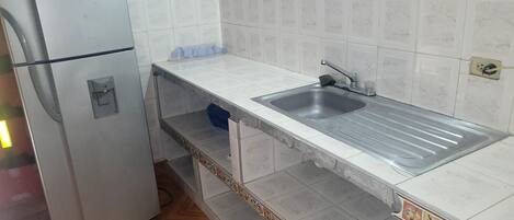 Una cocina con pileta de acero inoxidable, salpicadero de azulejos blancos y refrigerador.