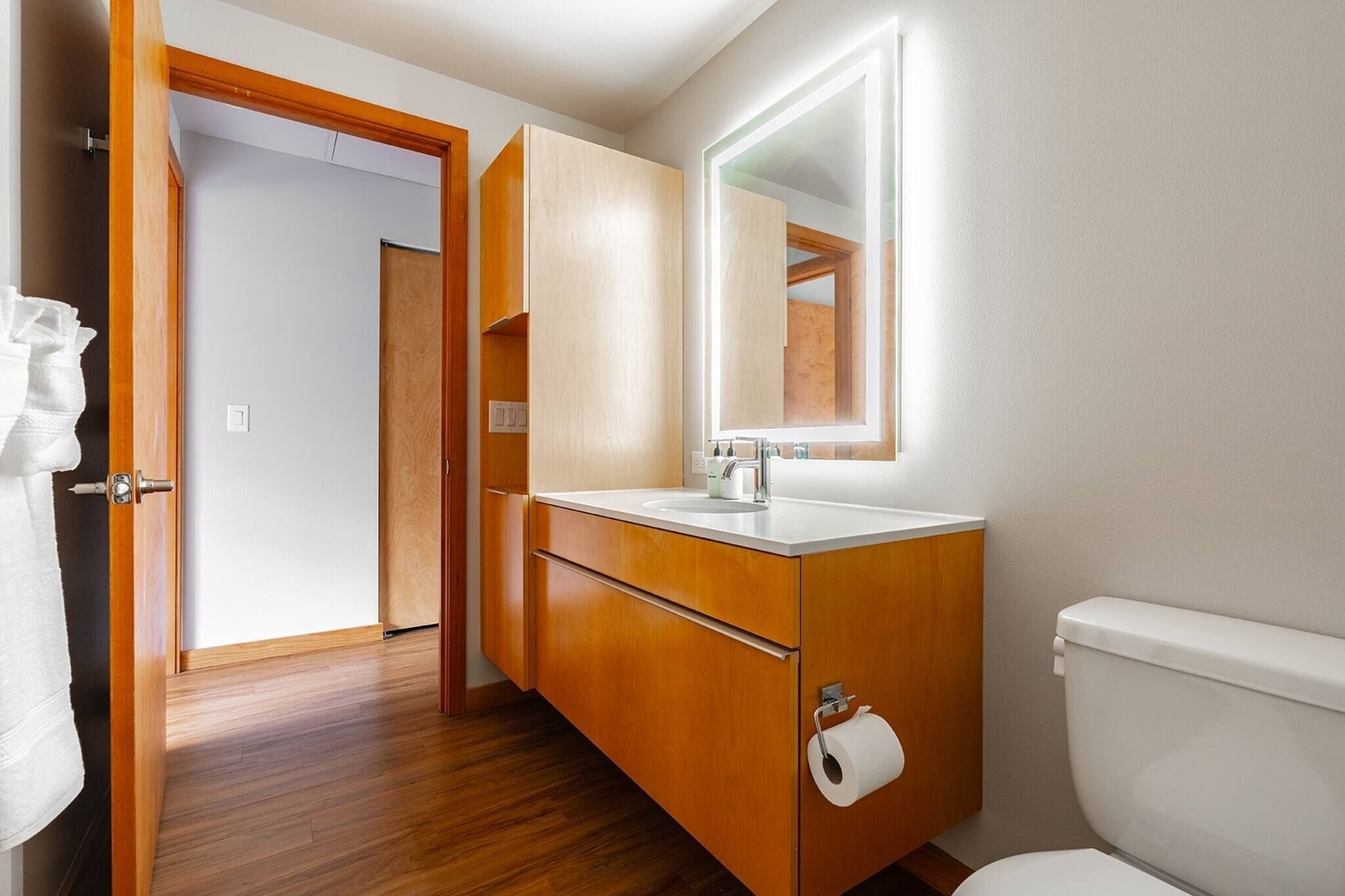 Een badkamer met houten kastjes, een witte wastafel, een spiegel en een toilet.