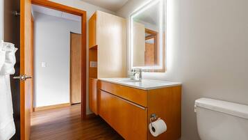 Een badkamer met houten kastjes, een witte wastafel, een spiegel en een toilet.