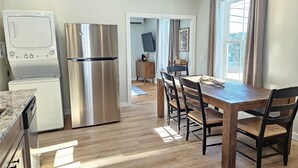 A modern kitchen with stainless steel appliances, a wooden dining table with chairs, and a view of the outdoors through a window. - 7 mins to Acadia, water view, & walk to town! (Southwest Harbor)