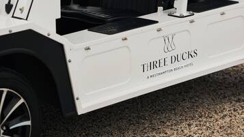En golfbil med svart tak och vit kaross, märkt med texten ”Three Ducks” och en logotyp ovanför texten.