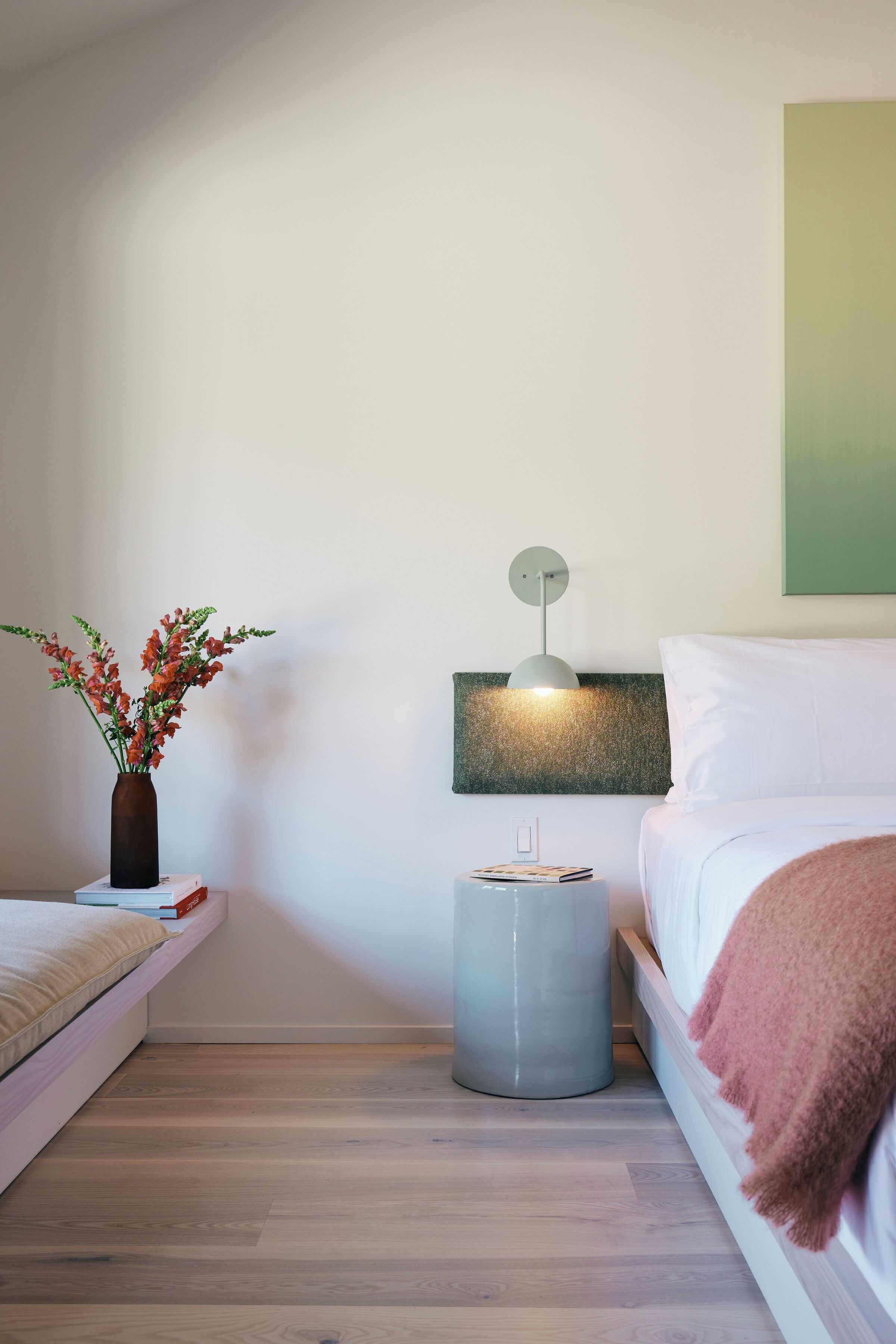 A neatly arranged bedroom with a bed, bedside table, lamp, and a vase of flowers.