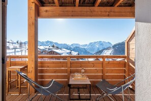 A wooden deck with a table and two chairs, overlooking a snowy mountain landscape. - Borealis - Cosy Apartment in Alpe d'Huez (Huez)