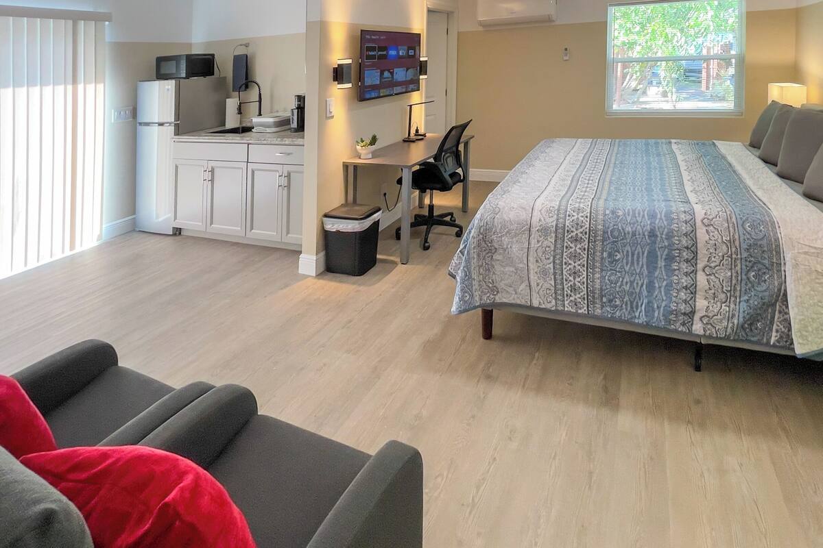 Ein modernes Hotelzimmer mit einem großen Bett, einem Schreibtisch, einer Küchenzeile und Blick auf Grün.