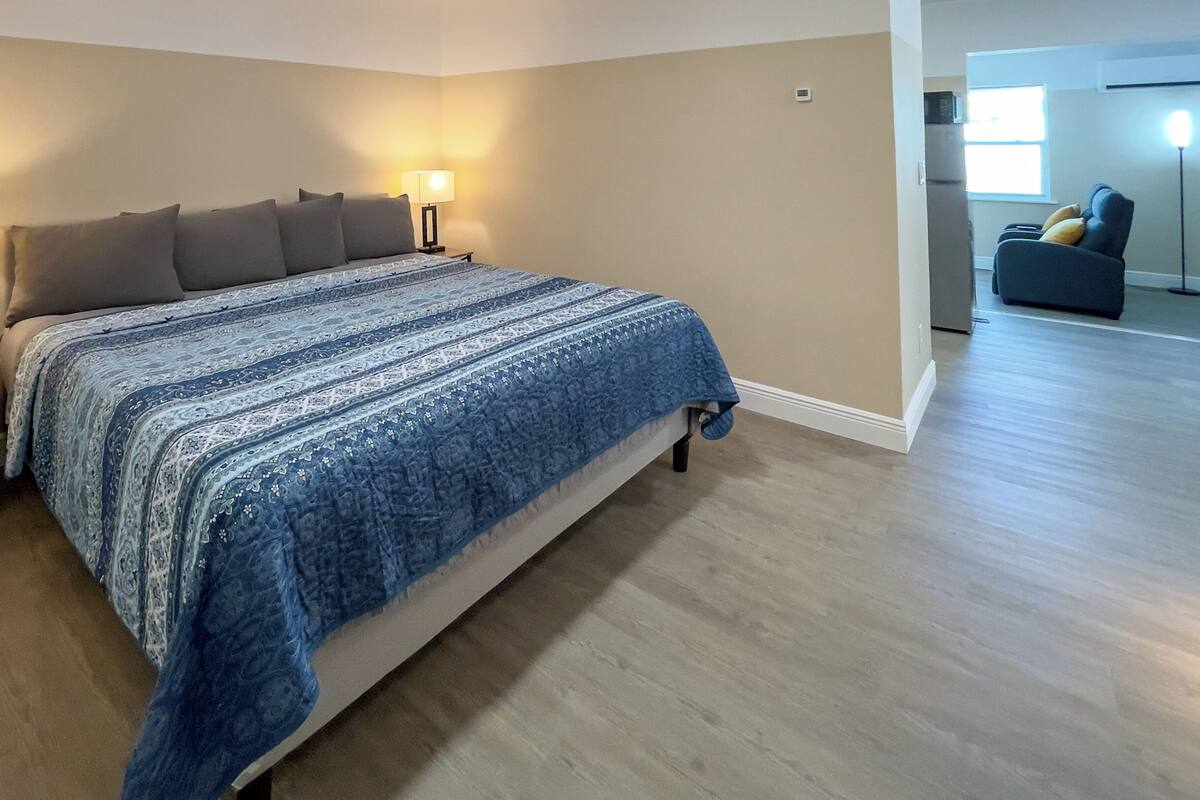 Ein Schlafzimmer mit einem Bett, zwei Nachttischen mit Lampen, einer Kommode und Blick auf den Wohnbereich.