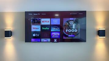 A TCL TV mounted on a wall displaying various streaming services.