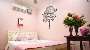 Une chambre avec un lit, un climatiseur fixé au mur, un motif décoratif représentant un arbre, un vase avec des fleurs et une petite table sur laquelle se trouve un panier.