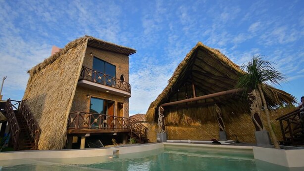 A resort with a pool, thatched-roof buildings, and a clear blue sky. - Norock Club and Beach (Copala)