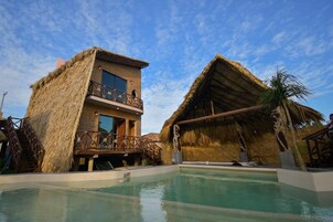 A resort with a pool, thatched-roof buildings, and a clear blue sky.