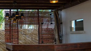 A wooden ceiling with hanging pendant lights, a brick floor, and a wooden counter with a small window. - Norock Club and Beach (Copala)