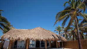 A thatched-roof structure with large windows, surrounded by palm trees and a sandy beach. - Norock Club and Beach (Copala)