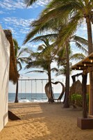 A beach setting with palm trees, a swing set, and a thatched structure.