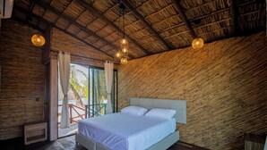 A bedroom with a large bed, wooden walls, and a thatched roof. - Norock Club and Beach (Copala)
