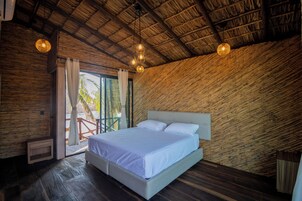 A bedroom with a large bed, wooden walls, and a thatched roof.