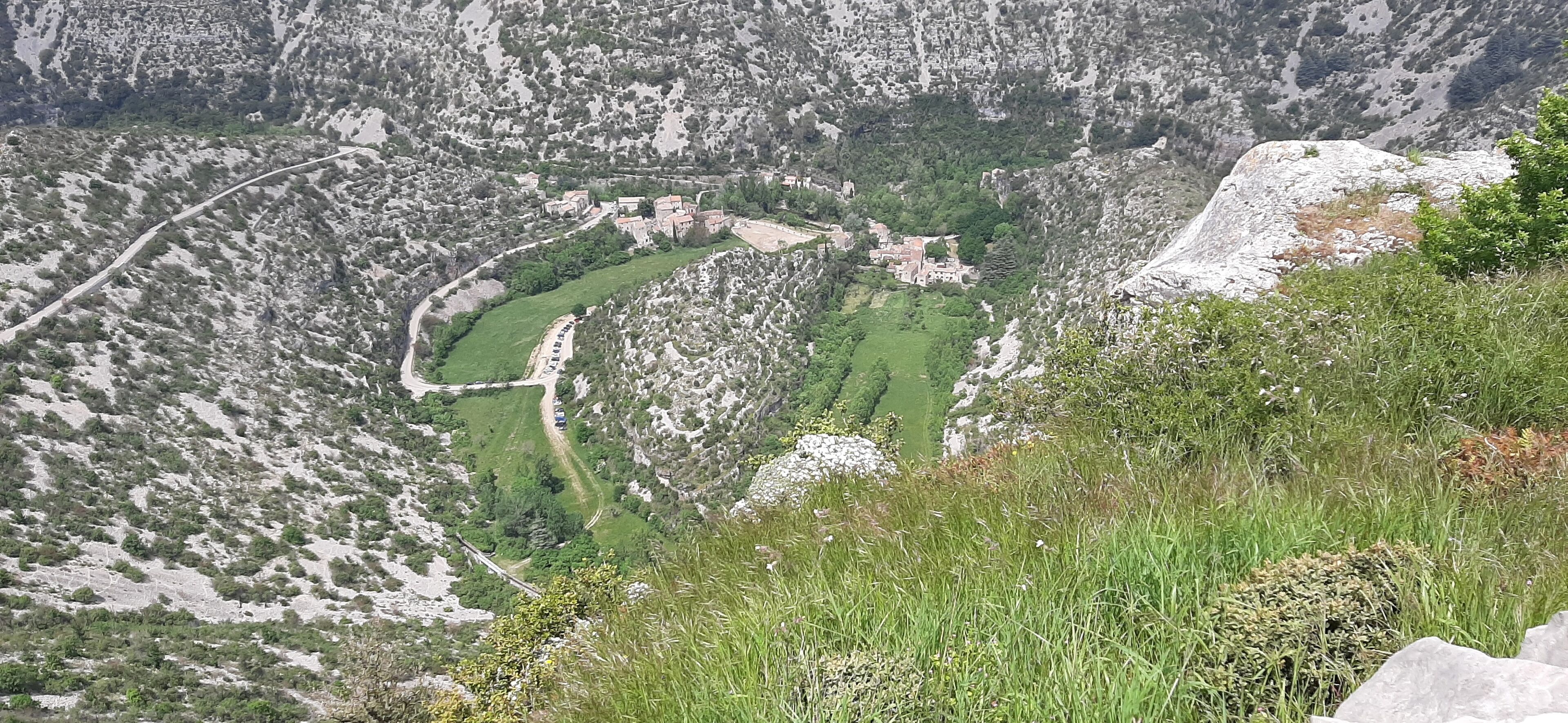 Et bjergrigt landskab med en snoet vej, grønne marker og en lille landsby med bygninger.