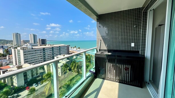 A balcony with a view of the ocean and cityscape, a tiled wall, and a small sink. - RN STUDIO - APTO 905 (Maceió)