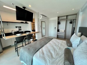 A modern hotel room with a kitchenette, a bed with a grey blanket, a bedside table, and a wardrobe. - RN STUDIO - APTO 905 (Maceió)