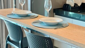 A dining table set with two plates and two wine glasses, with a kitchen area in the background. - RN STUDIO - APTO 905 (Maceió)