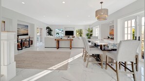 A spacious living room with a white sofa, a dining table with chairs, a TV, and a large window. - Playa Palma Private Pool Home 4 Minute Walk to Holmes Beach on AMI (Holmes Beach)